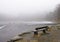 Lonely wooden bench in winter scenery by frozen lake in foggy rainy weather, bergen, norway