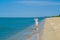 A lonely young girl in a swimsuit and sunglasses stands on the sand near the surf on an empty sea beach. Bright sunny