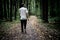 Lonely young male hipster in casual walks in autumn dark moody forest with fallen leaves