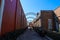 A long alley way between two red brick buildings with metal arches along the alley with lush green plants and a gorgeous blue sky