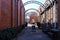 A long alley way between two red brick buildings with metal arches along the alley with lush green plants and a gorgeous blue sky