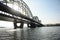 A long arched iron bridge over a wide river. A sun breaks through it