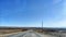 Long asphalt road stretching to the horizon. Fields on the roadsides and old electric poles on a sunny day wtih blue sky