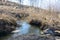 Long-awaited spring creeks flow over ravines and hills on a sunny day. Water rapids and waterfalls of streams among the dry grass