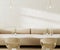 Long beige sofa in cafe interior with coffee tables and chairs, empty white stone wall, 3d rendering