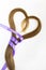 Long blond hair donation put like heart with lavender ribbon as symbol of fight against cancer on white background. Top view.