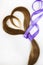 Long blond hair donation put like heart with lavender ribbon as symbol of fight against cancer on white background. Top view.