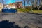 Long blue dumpster on a street by a curb near residential home.