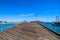 A long brown wooden pier with a gray metal hand rail and tall lamp posts along the pier surrounded by deep blue ocean water