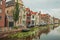 Long canal with aquatic plants, brick houses on its bank and cloudy day at Gouda.