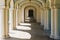A long corridor in classical architectural style with many elegant columns and arches leading in perspective to a door