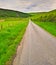 Long country road between green fields, hills and forest