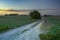 Long country road through green fields after sunset