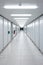 Long empty illuminated interior hallway. Vanishing perspective, bright neon lights, vertical cabinets lined side wall. Underground