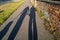 Long evening shadows of a man and woman walking the dog on a leash at golden hour dusk.