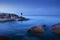 long exposure of blue sea scape at morning light with man fishing on rock