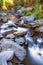 A long exposure image of a mountain river milky white flowing over blue-grey rocks, soft-focus glowing sunlight, and trees with