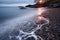 a long exposure image of waves washing over pebbled shoreline