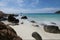 Long exposure of light waves rolling over large rocks in a idilic white sand beach in a small bay with small islands on