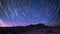 A long exposure photograph of the desert at night with the stars leaving trails of light across the sky. The stillness