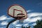 A long exposure photograph of a dirty orange and white playground basketball hoop, rim and net with motion blurred clouds in a