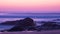 Long exposure shot at dusk over ocean with rocks in foreground and milky waves behind.