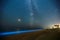 Long exposure shot of glowing plankton on sea surf and milky way. Blue bioluminescent glow of water under the starry sky