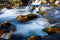 Long exposure of a small stream gently flowing over rounded rocks