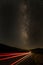 Long exposure traffic trails from tail lights stretching down the road toward the milky way