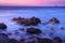 Long exposure of waves on rocky beach with purple sunset background