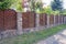 Long fence of wood and brown stone on the street in the grass