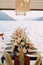 Long festive table with flowers and chairs stands on a pier by the sea