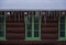 Long Gnarly Icicles Hand Down From Log Cabin Over Green Windows