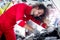 Long hair handsome mechanic man in red uniform works with engine vehicle, auto mechanic technician inspecting maintenance engine