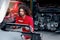 Long hair handsome mechanic man in red uniform works with engine vehicle, auto mechanic technician inspecting maintenance engine