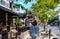 Long haired boy walking down sidewalk past resturants and tropical trees with bicycle riders and other tourists in Key West