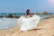 Long-haired brunette bride runs along the sandy coastline on the background of stones in the sea, the beach on the Indian Ocean.