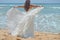 Long-haired brunette bride straightens her dress standing on the sand, girl looks up at the sky on beach on the Indian Ocean. Wedd