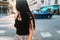 Long-haired brunette girl in black tank-top walking across the street exploring new town somewhere in Europe. Outdoor