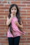 Long-haired Colombian girl adjusts her hair next to a brick wall