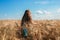 A long-haired fair-haired girl walks in a golden field of rye. View from the back. The freedom and joy of being in nature. Summer