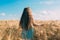 A long-haired fair-haired girl walks in a golden field of rye. View from the back. The freedom and joy of being in nature. Summer