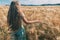 A long-haired fair-haired girl walks in a golden field of rye. View from the back. The freedom and joy of being in nature. Summer