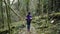 Long-haired girl in a sports jacket goes on a forest trail past the mysterious trees covered with green moss.