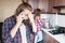 A long-haired man is upset talking on the phone or calling a food and drug delivery service home standing in the kitchen