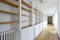 Long hallway of a home with a long empty bookcase with wooden shelving and a loose oak floor