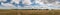 A long horizontal panorama with an agricultural field and beautiful sky and clouds. A haystack left in the field after harvesting