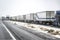 Long line of out of service big rigs semi trucks with loaded semi trailers standing on the highway shoulder due to a snow storm in