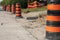 long line row of orange and black traffic delineator pylon barrel drums