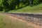 Long low rusticated stone block retaining wall in an outdoor park, green hillside and trees beyond